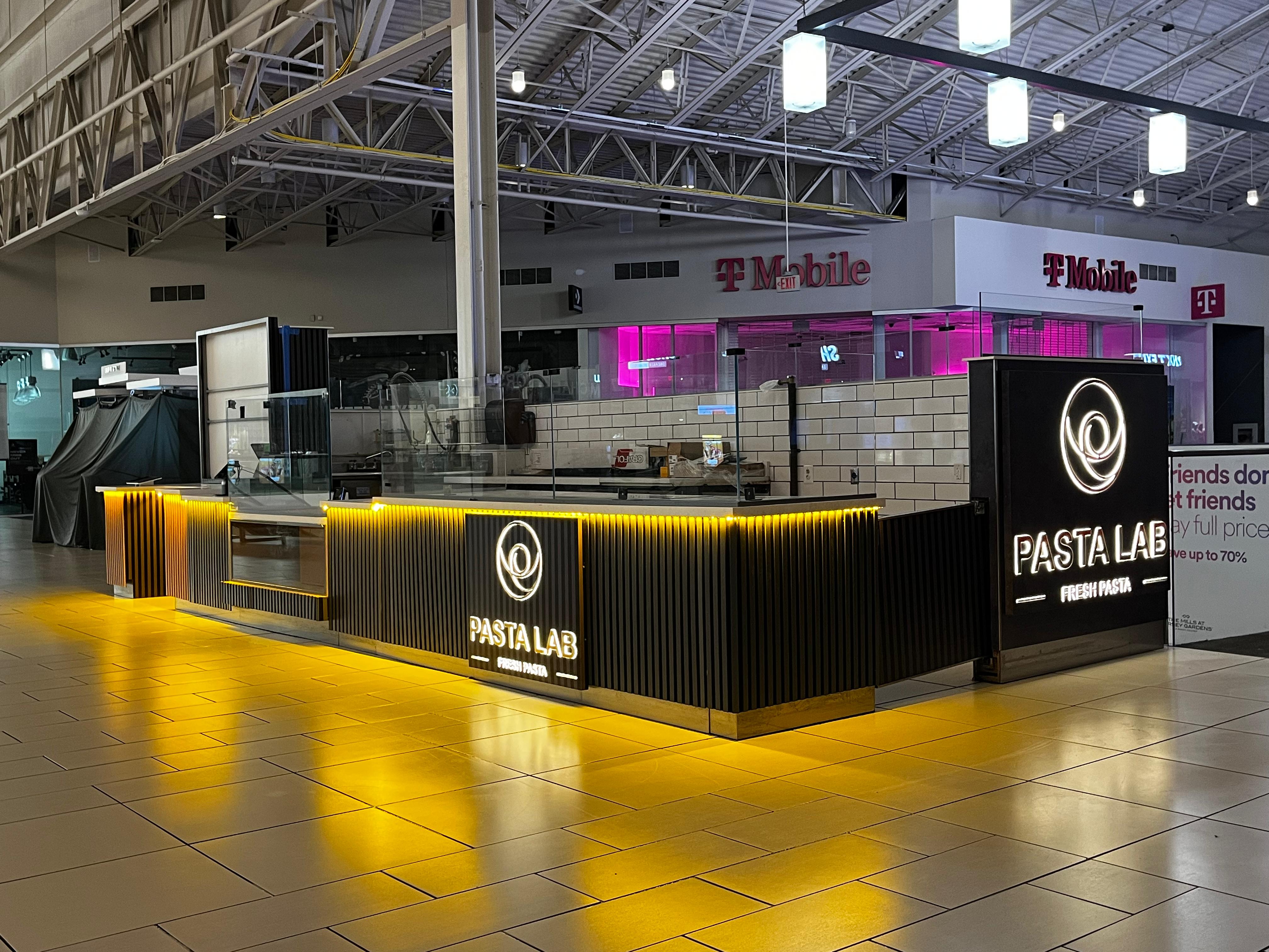 Pasta Lab kiosk — dark black millwork with gold accents and illuminated brand panel