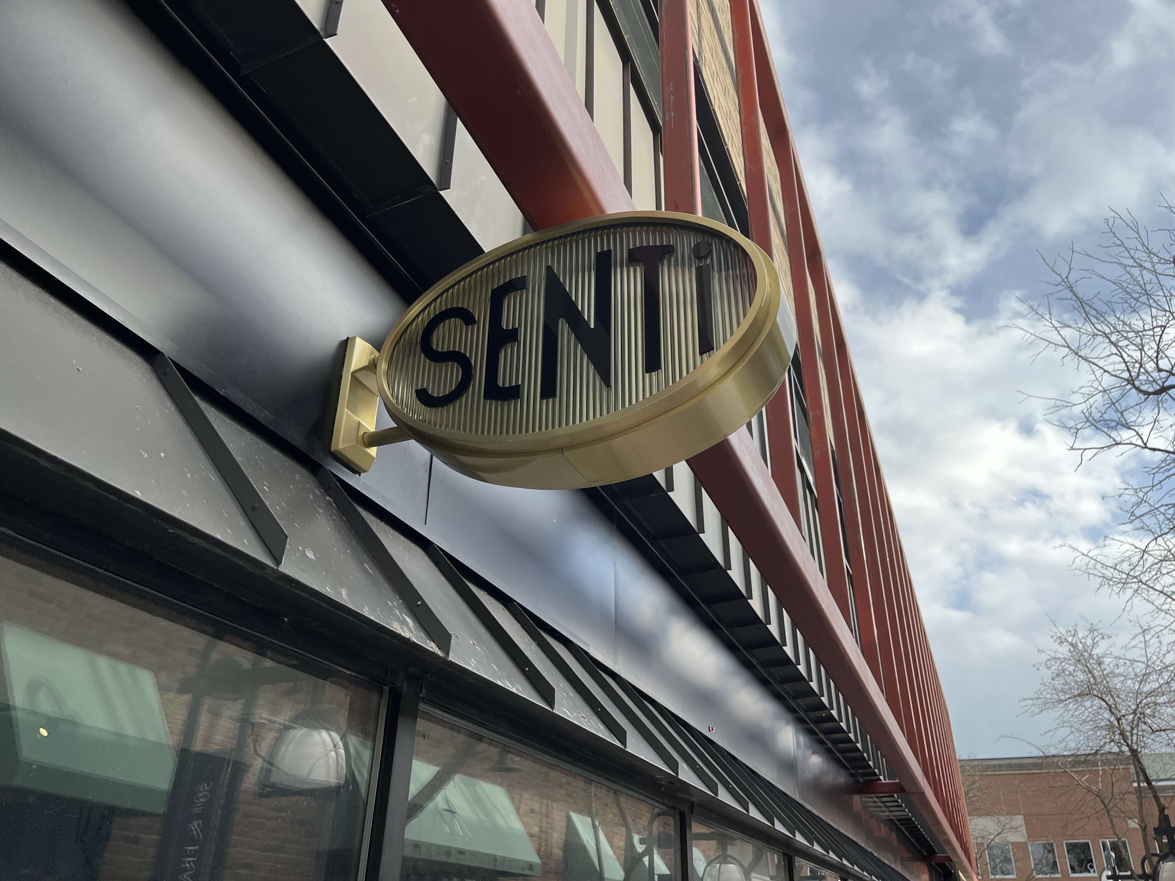 SENTi gold dimensional oval blade sign mounted on a building exterior